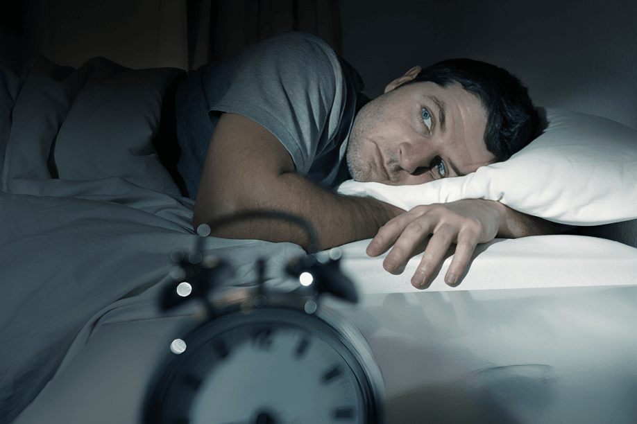 A man lying in bed, looking at the alarm clock.