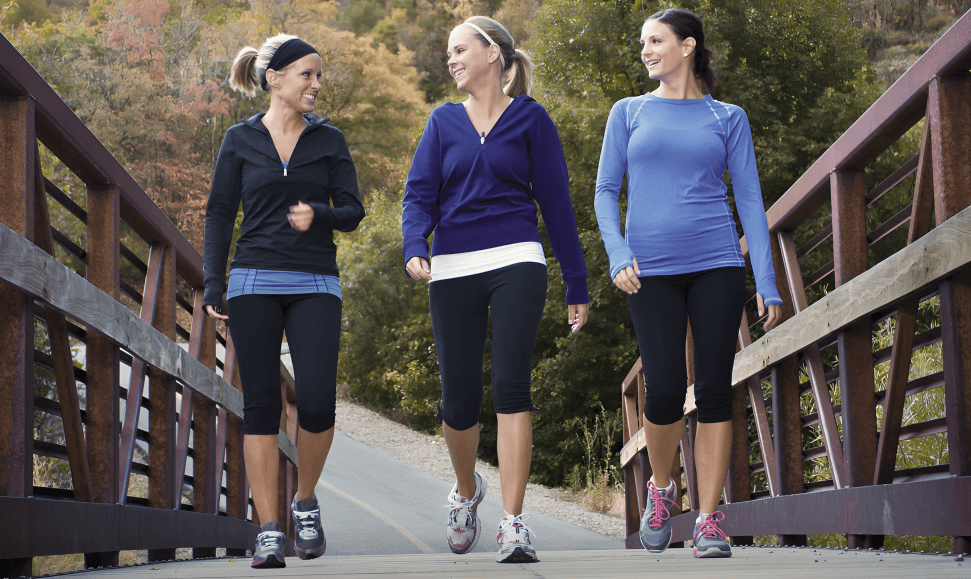 Three women jogging happily across a wooden bridge.