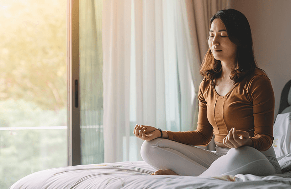 Woman with closed eyes meditating on a bed.