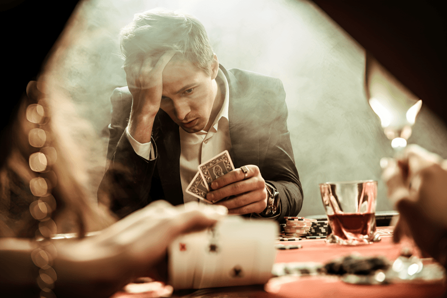 Man stressed while playing cards at a smoky table.