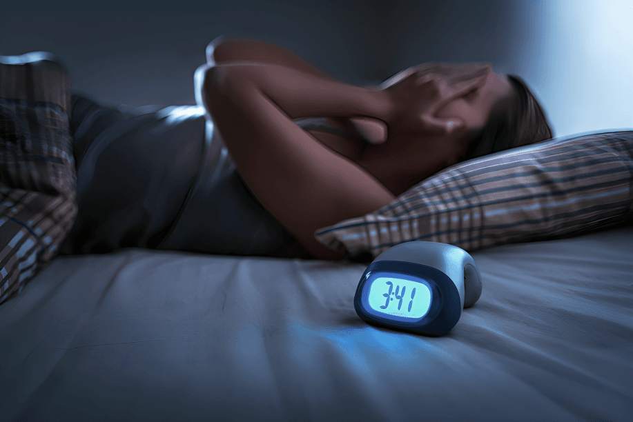 A person lying awake in bed with an alarm clock.