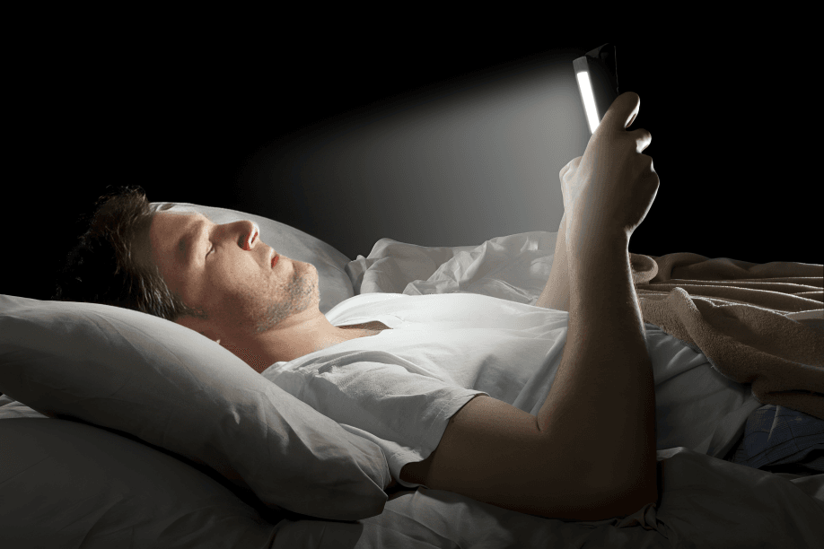 Man in bed looking at bright phone screen.