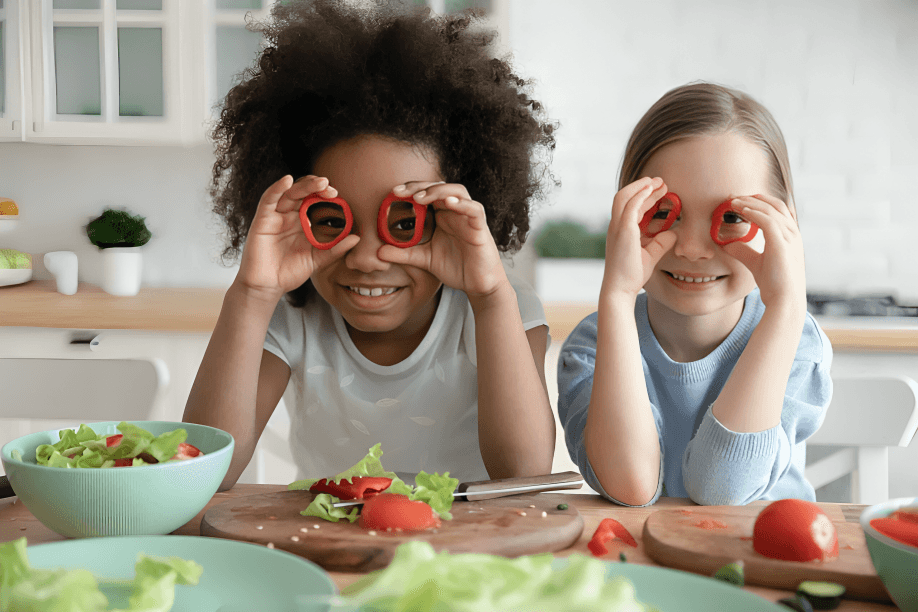 Two smiling girls hold pepper slices over their eyes.