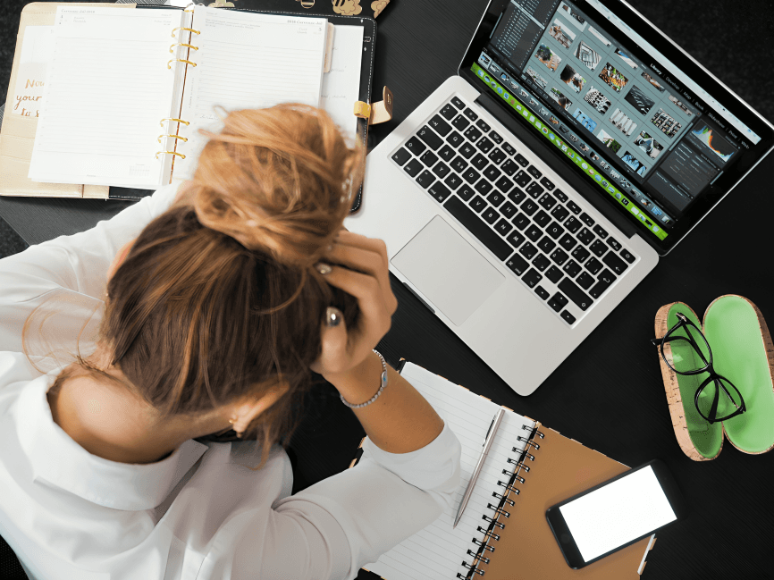 An overwhelmed person at a desk with a laptop and a planner.