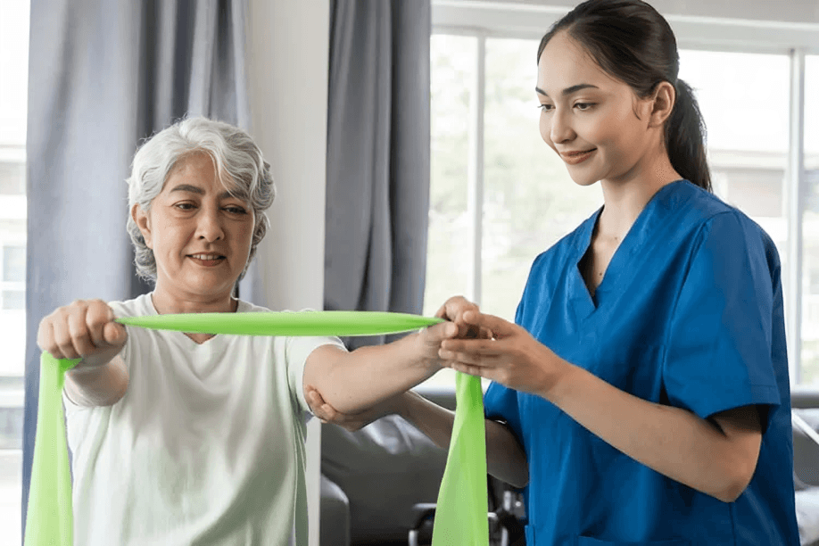 A physiotherapist helps smiling elderly woman with resistance band.