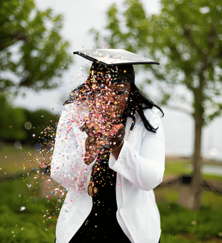 Graduate in cap and gown showered with confetti outdoors.