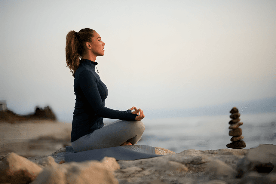 A woman meditating by the sea at sunrise.