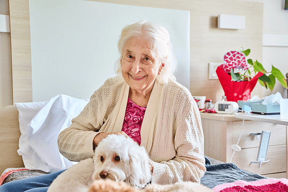 Elderly woman smiles, petting a white dog.