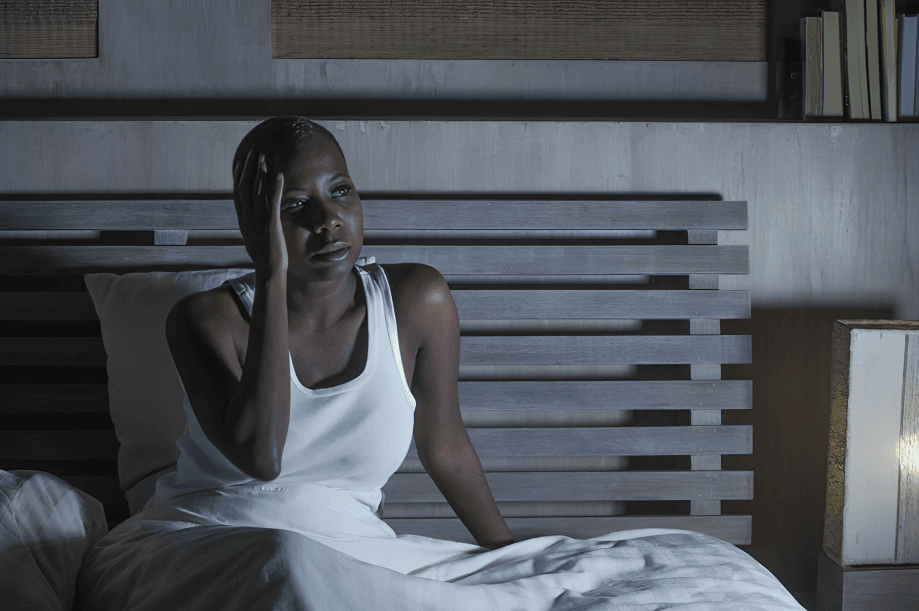 A person with short hair sits awake in bed.