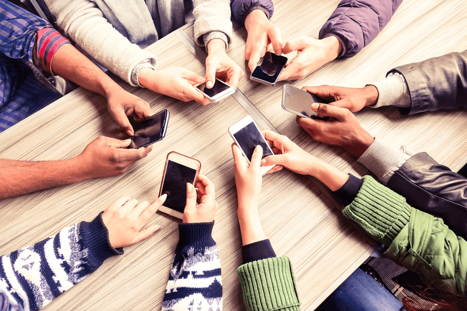 Diverse hands holding and using smartphones around a table.