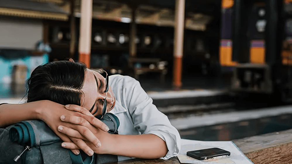 Woman asleep on her backpack at a train station.