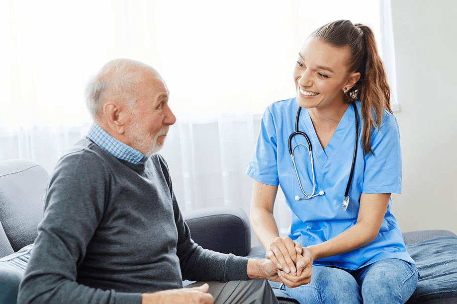 A nurse smiles, holding an elderly man's hand.