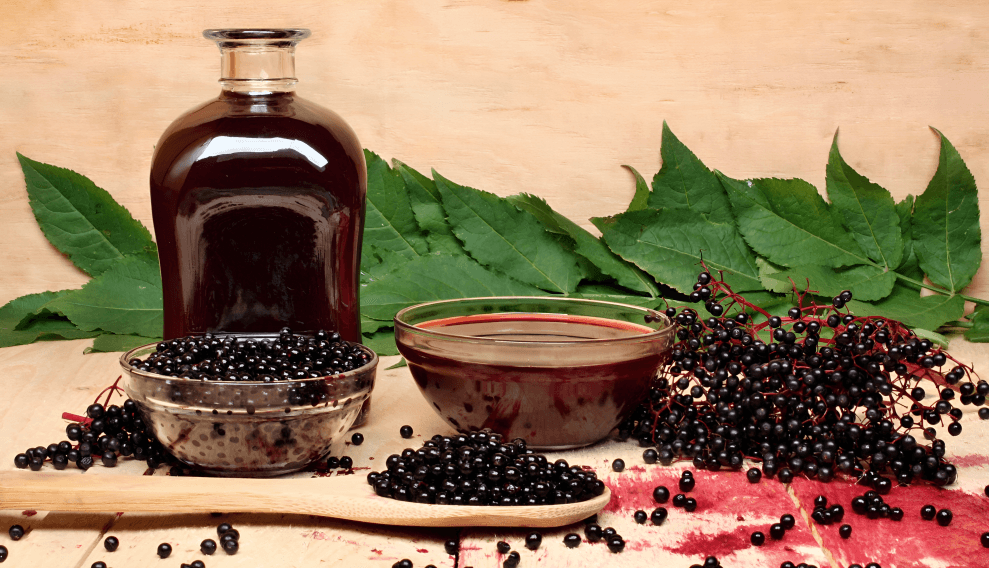 Elderberry syrup, fresh berries, and leaves on wood.