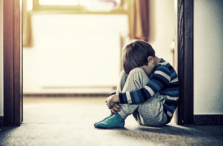 A child sits alone, hugging knees, looking sad.