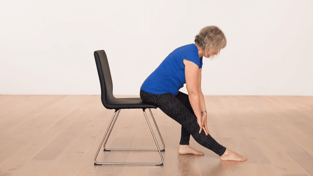 Woman on chair stretching leg, side view.