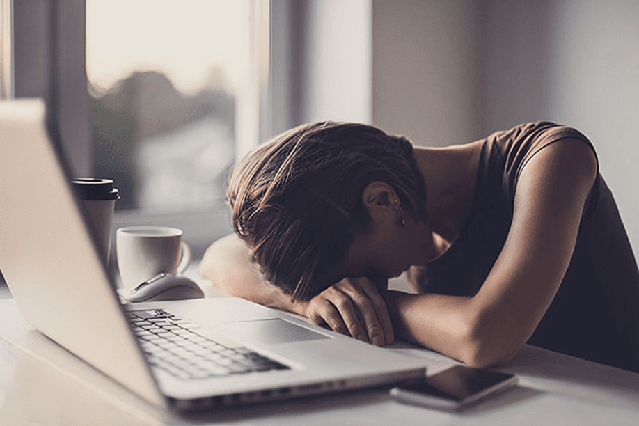 An exhausted person slumped over a laptop at the desk.