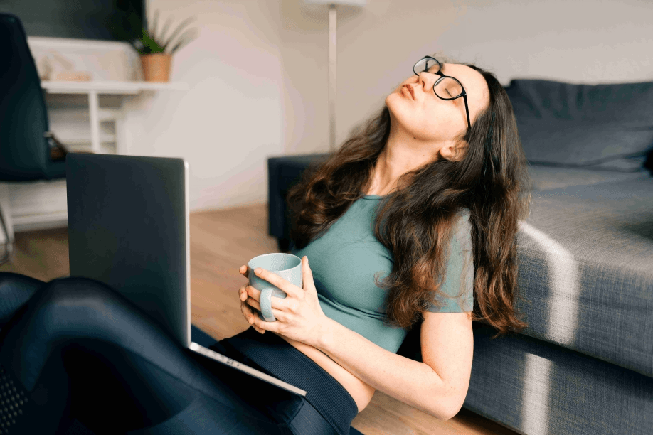 Woman leans back with laptop and coffee indoors.