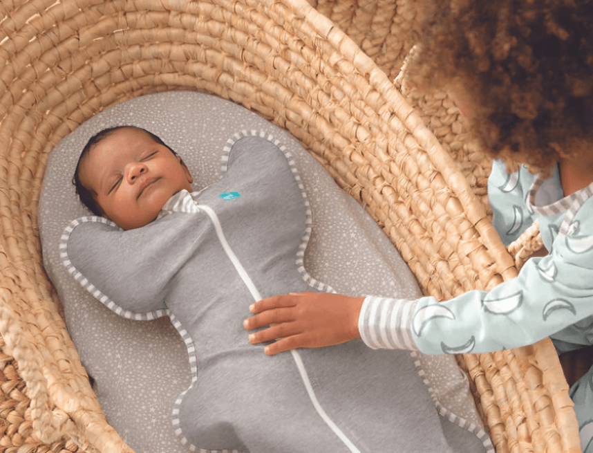 A child gently touches a sleeping baby in a swaddle.