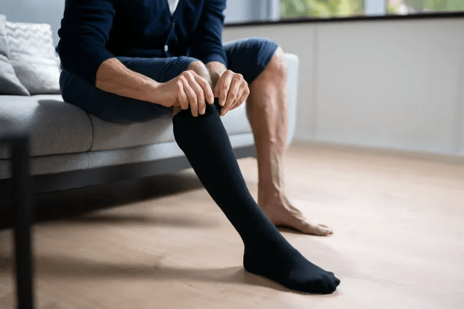 A man putting on a black compression stocking.