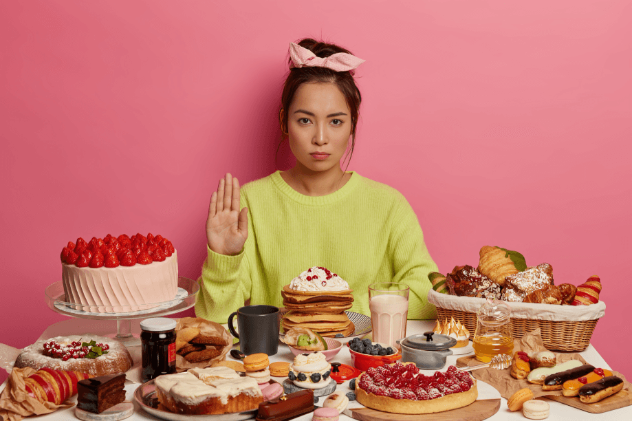 A young woman rejects sweets and pastries on a table.