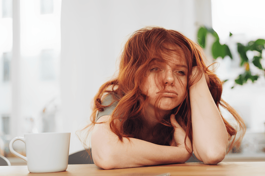 Tired-looking woman with red hair resting at a table.