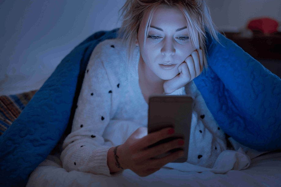 The woman in bed looks at her bright smartphone screen.