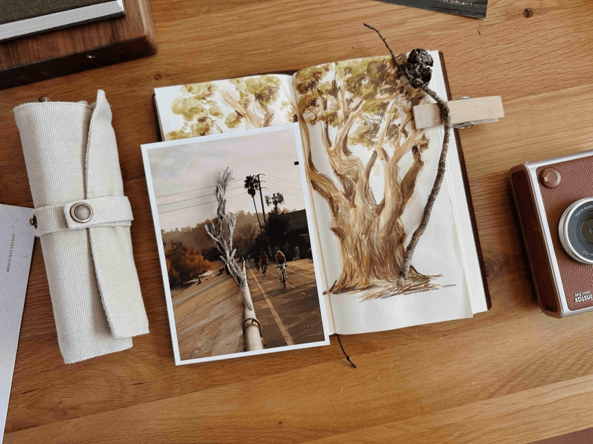 Open sketchbook with tree drawing and photo on desk.