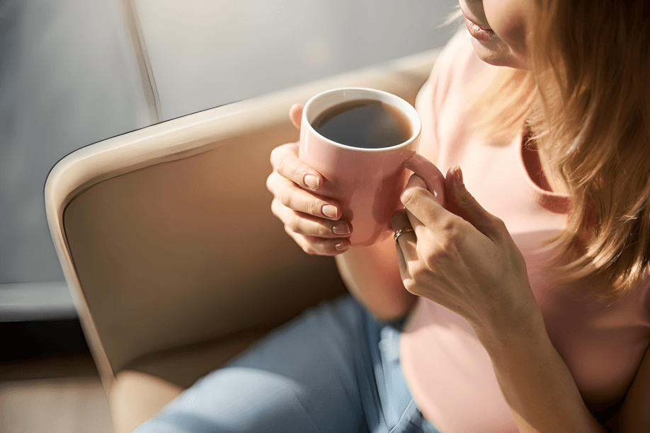 Woman holding pink mug with coffee, seated.