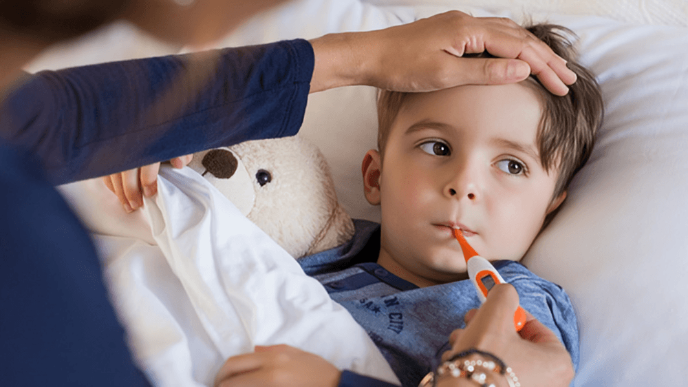 A child with a thermometer and hand on forehead.