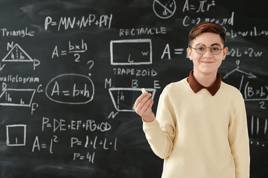 A smiling student in glasses stands before a chalkboard.