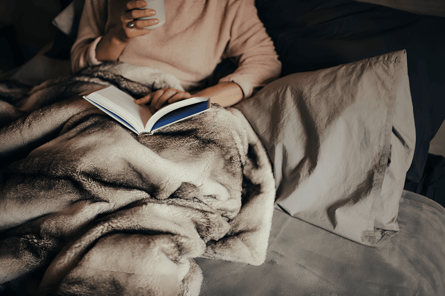 Cozy reading in bed with a warm drink.