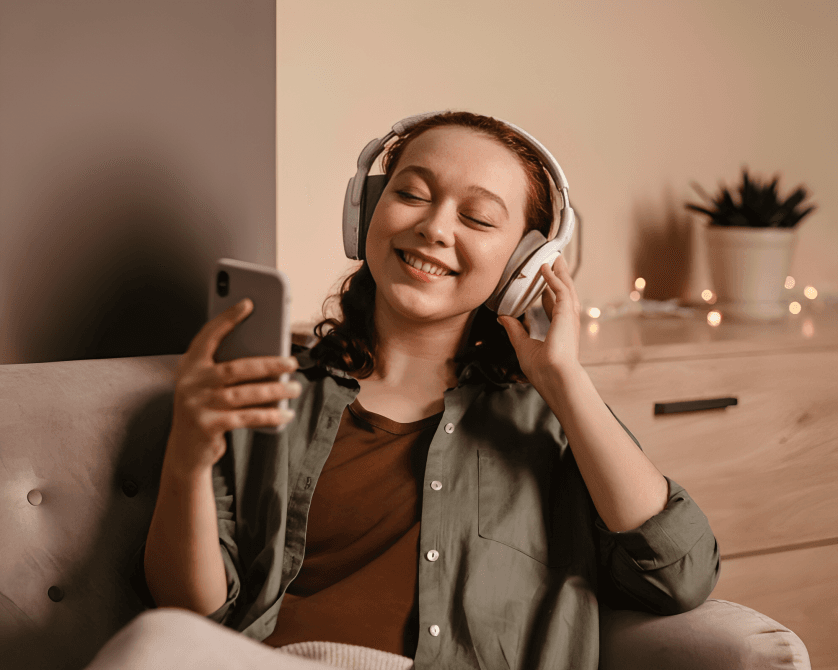 A smiling woman with headphones looks at her smartphone contentedly.