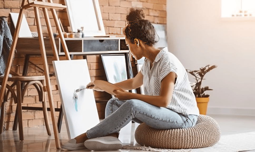Artist painting on canvas in a sunlit studio.