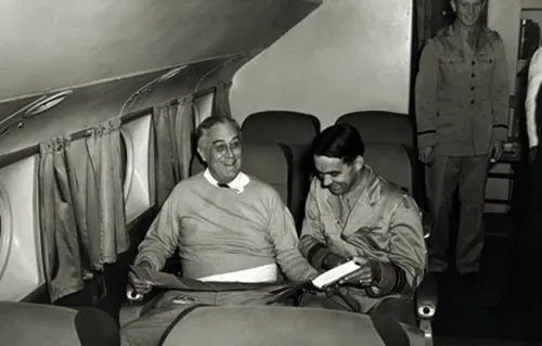 President Franklin D. Roosevelt smiling and talking mid-flight with a young man on an airplane.